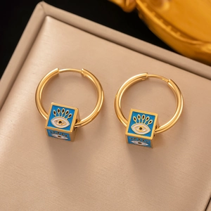 Schicke goldene Creolen mit blauen Evil Eye Anhängern auf beigem Ledertextur-Hintergrund