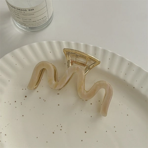 Detailed shot of beige marble acetate hair claw with a wavy shape on a ceramic tray