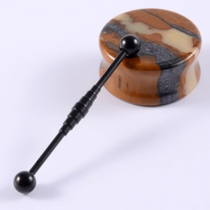 Macro shot of black industrial barbell and striped stone ear plug on white surface