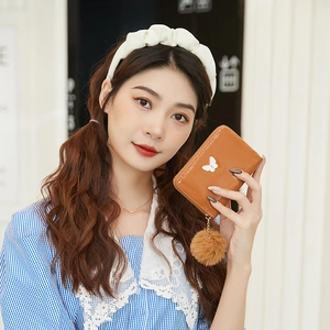 Brown fashion wallet with white butterfly ornament and plush pompom charm held by model