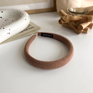 Close-up of brown knitted headband with white handmade label on natural white desk