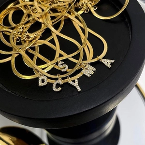 Detailed view of layered gold snake chains with rhinestone-encrusted initial pendants