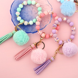 Pastel beaded keychain bracelet with soft pompom and leather tassel on pink background