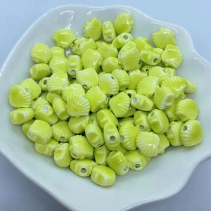 Macro shot of glossy yellow shell-shaped ceramic beads with holes in a white lace plate