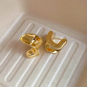Macro shot of polished gold-plated irregular C-shape metal earrings with textured background