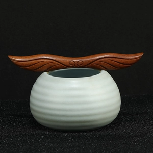Creative celadon ceramic tea canister with finely carved dark wood wing lid on black background