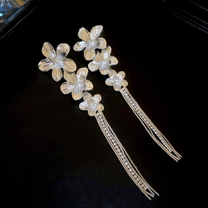 Close-up of silver flower drop earrings with long tassel chains and crystal accents