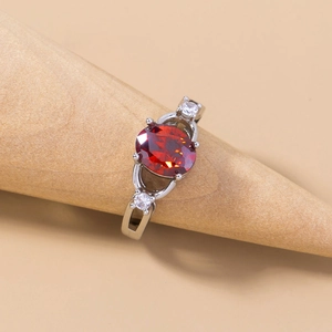 Detailed view of a silver ring with a red round-cut gemstone on a wooden display stand
