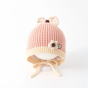 Detail of pink knitted baby hat featuring beige bow, floral accent and cotton lining