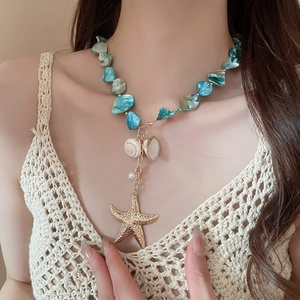 Macro view of blue beaded necklace featuring a gold starfish and white seashell pendant