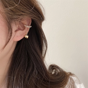 Dettaglio di un ear cuff dorato con perle eleganti e un ciondolo a cuore con nappa sottile