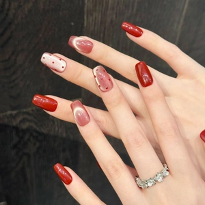 Short square press-on nails with red cat-eye effect and polka dots on dark wood backdrop