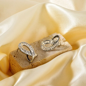 Elegant twisted silver earrings with baguette zircons on golden satin fabric background