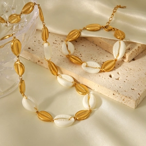 Detail of a golden chain necklace with white shell charms on beige stone and silk background