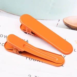 Close-up of two bright orange metal hair clips with smooth painted finish on a card