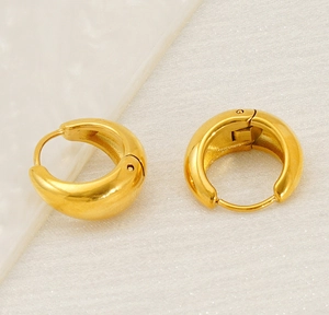 Detailed close-up of chunky gold hoop earrings on a minimalist marble background