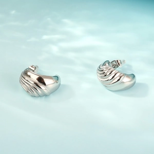 Macro view of silver C-shaped earrings featuring a shell-like textured wavy surface