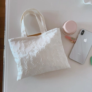 Detail of white floral jacquard handbag with texture and elegant double handles