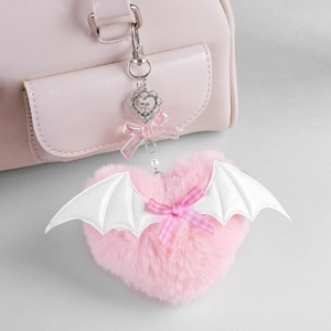 Pink plush heart charm with white wings and metal cross keychain on a pink bag