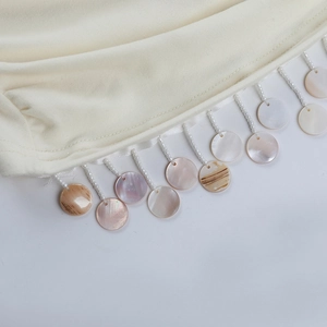 Détails de la frange de robe en maille crème avec perles et coquillages irisées