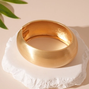 Close-up of golden wide metal bracelet with brushed matte finish on stone base