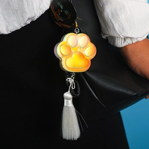 Detailed close-up of iridescent cat paw pendant with white tassel on black leather bag