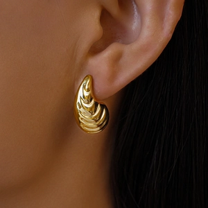 Gros plan de boucles d'oreilles dorées géométriques en acrylique avec texture ondulée