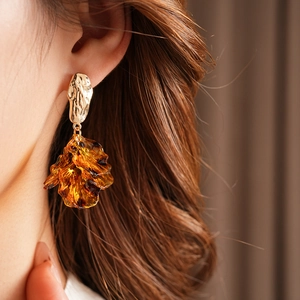 Detail of golden metal stud earrings with amber resin leaf pendant on model