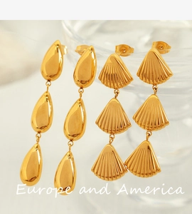 Close-up of golden teardrop and shell dangle earrings with a triple-layered metallic finish