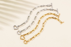 Detail of paperclip chain bracelets in gold and silver with heart charms and OT clasps