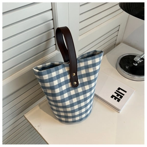 Detail of blue plaid canvas bucket bag with dark brown leather handle and gold rivets