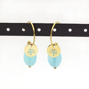 Detailed view of Tree of Life gold earrings with light blue stone drops on a stand