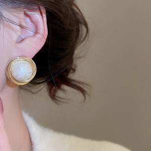 Close-up of elegant gold pleated geometric stud earrings with center white pearl on model