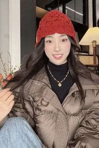 Détail d'un bonnet en maille torsadée rouge porté avec une doudoune marron brillante et collier