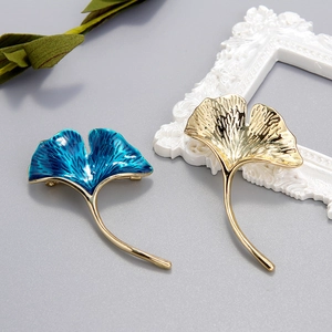 Ginkgo leaf brooches in gold and blue enamel finish on a minimalist elegant background