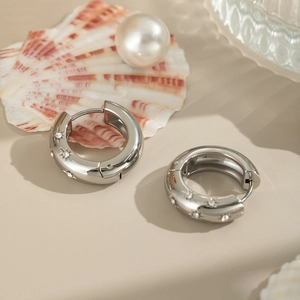 Detail view of silver C-shaped earrings with star patterns and inlaid zircons on a table