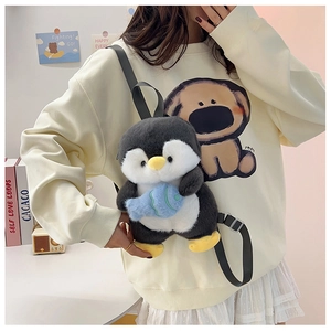 Detail of cute plush penguin backpack with small blue fish accessory worn by model