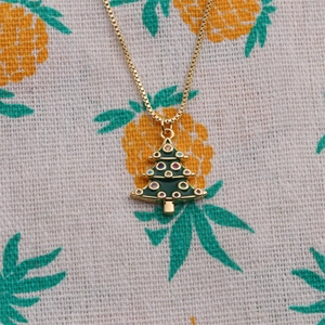Close-up of gold-plated Christmas tree necklace with green enamel and colored crystals