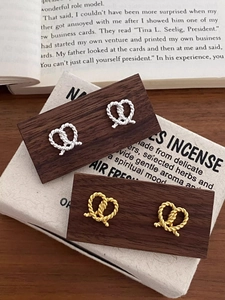 Detailed view of silver and gold twisted knot stud earrings on a vintage wooden stand