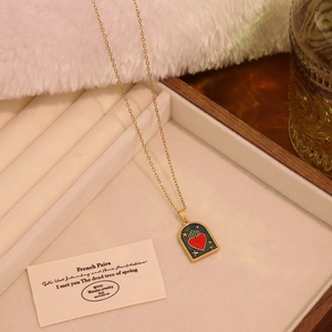 Detail of a vintage arch pendant with a red heart and green enamel stars on a gold necklace