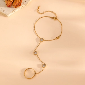 Detail of 18k gold plated slave bracelet with three heart-shaped white gemstones and ring