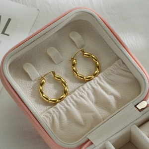 Détail de boucles d'oreilles torsadées dorées dans un coffret à bijoux en velours rose