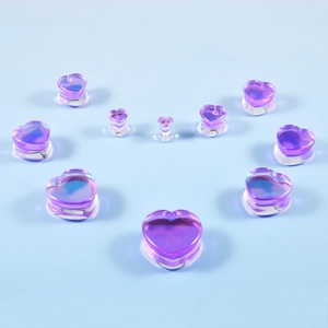 Multiple sizes of heart-shaped purple glass ear plugs arranged on a light blue background