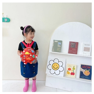 Toddler modeling a red dinosaur print backpack in a stylish indoor setting