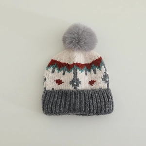 Dettaglio del cappello in maglia invernale con motivi Fair Isle e pompon grigio morbido