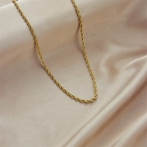 Minimalist gold plated twist chain necklace laid on elegant champagne silk fabric