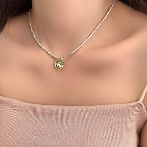 Detail of a gold-plated necklace with hammered round pendant on a textured chain