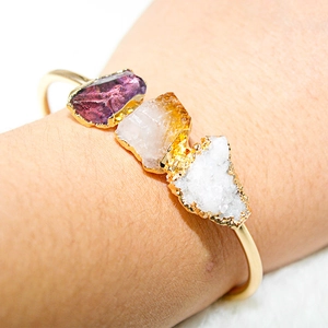 Detail of gold plated open bangle featuring raw amethyst and citrine crystal clusters