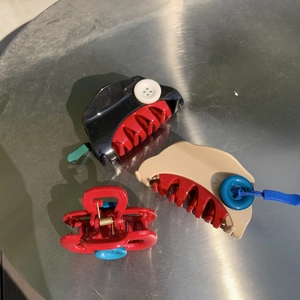Detailed view of three plastic hair claws in red, black, and beige with button accents