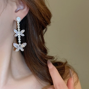 Detail of silver butterfly tassel earrings with zircon stones worn by a model in soft light